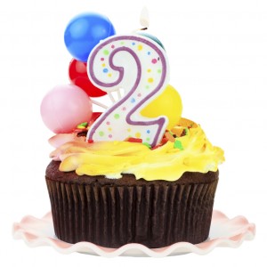 Chocolate birthday cake with number two candle and plastic balloons. Isolated on a white background.